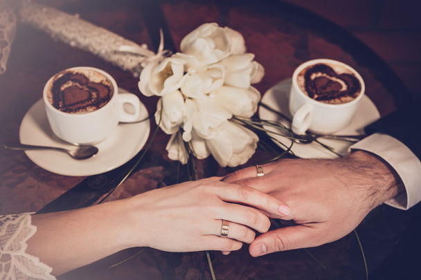 Twee kopjes koffie en hand van bruid en bruidegom met trouwringen - Foto, afbeelding