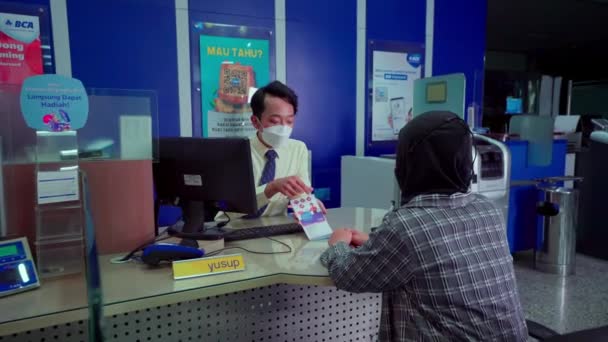 Bank employee in a mask discussing documents with a customer at a desk in a bank office. - Footage, Video