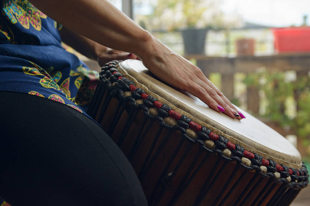 Closeup of Female Hands on the leather head of a Djembe drum of a unrecognizable woman at home. Closeup side view image of woman playing, practicing at home, copy space - Photo, Image
