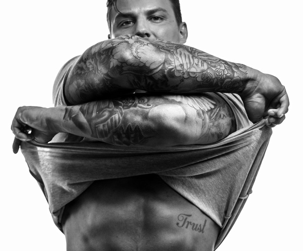 Man with tattooes undressing on white background - Photo, Image