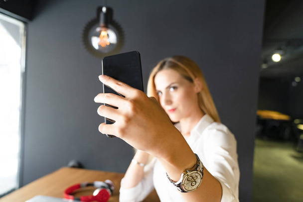 Bizneswoman robi sobie selfie komórką siedząc przy biurku - Zdjęcie, obraz