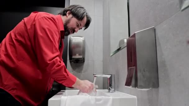 Hombre lavándose las manos en el baño público, un hombre con una camisa roja se lava las manos en un baño público - Metraje, vídeo