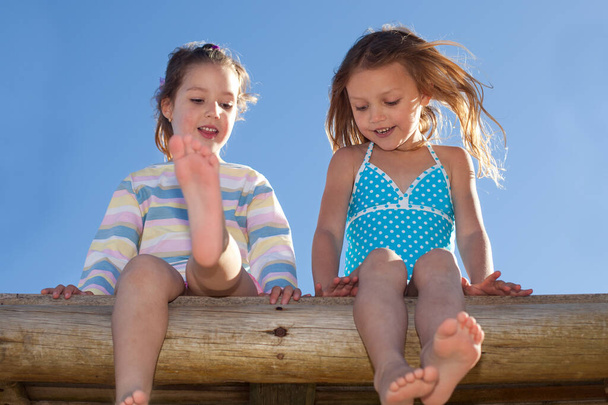 zwei süße kleine Mädchen sitzen nebeneinander und genießen den sonnigen Tag - Foto, Bild