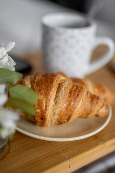 Desfrute de uma manhã acolhedora com uma bandeja de pequeno-almoço na cama, com croissants franceses frescos, café e uma pequena flor. - Foto, Imagem