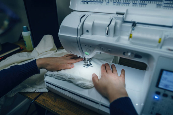 Vue rapprochée des mains féminines utilisant une machine à coudre moderne, démontrant la précision requise pour coudre le tissu - Photo, image