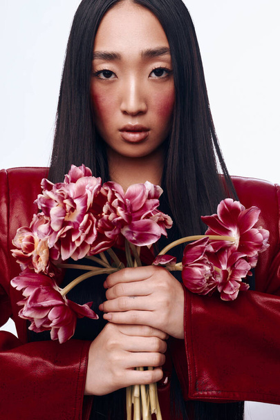 Beautiful Asian Woman in Red Leather Jacket Holding Bouquet of Pink Flowers Outdoors by Urban Wall - Photo, Image