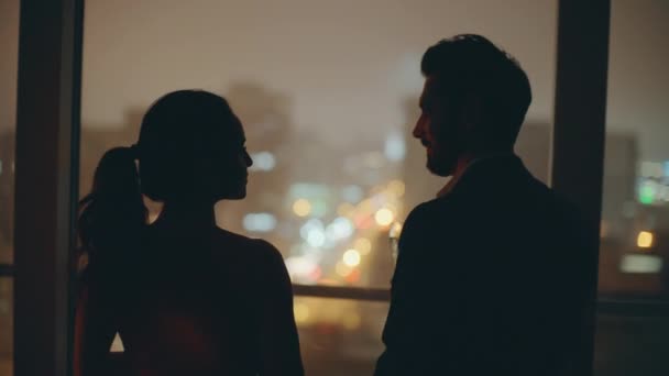 Romantic spouses silhouettes celebrating anniversary watching night lights city window closeup. Back view man woman toasting glasses at panoramic room. Beautiful lovers enjoying evening time together - Footage, Video