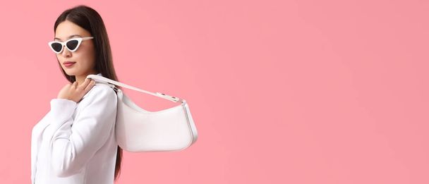 Красива молода азіатка зі стильною сумкою та сонцезахисними окулярами на рожевому фоні з простором для тексту - Фото, зображення