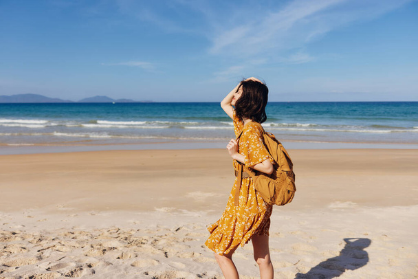 Kuva naisesta keltaisessa mekossa rannalla selkä mereen päin aurinkoisena päivänä - Valokuva, kuva