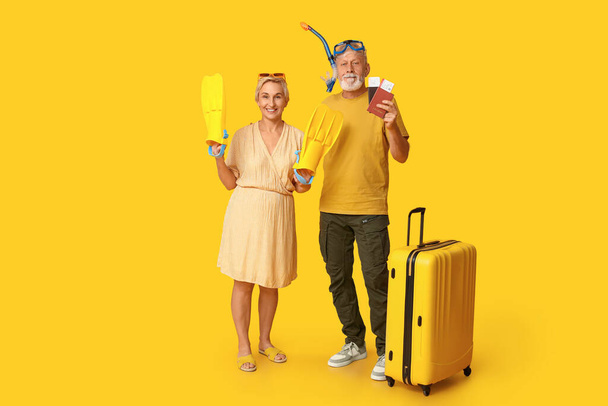 Ζευγάρι ώριμο με αξεσουάρ κατάδυσης και βαλίτσα σε κίτρινο φόντο. Ταξιδιωτική έννοια - Φωτογραφία, εικόνα
