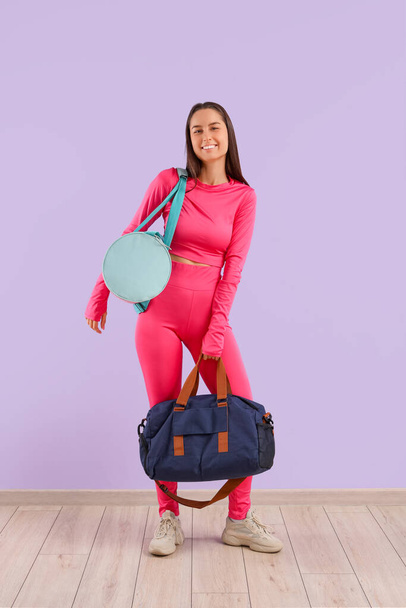 Sportieve jonge vrouw met tassen op lila achtergrond - Foto, afbeelding