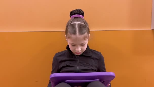 Genesteld in een rustige gang, vindt deze toegewijde jonge kunstschaatser een moment van rust, verdiept in haar tablet terwijl ze zich mentaal voorbereidt op haar komende optreden.. - Video