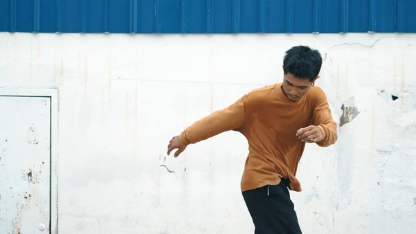 Hispanic man stretch arms and dance break dancing in front of wall. Motion shot of stylish street dancer in casual outfit practicing dancing in hip hop style. Outdoor sport 2023. Background. Endeavor. - Photo, Image