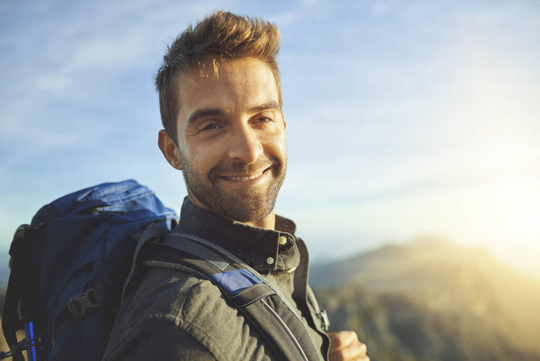 Portrait, mountains and hiking with man, journey and happiness with nature, sunshine and getaway trip. Face, person and hiker with backpack, adventure and travel with wellness, holiday and fitness. - Foto, Imagen