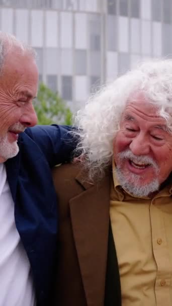 Vertical of three mature caucasian men enjoying embracing walk together laughing outdoor. Senior male old friends having fun hugging strolling happy in a urban city street. Elderly people golden ager - Footage, Video