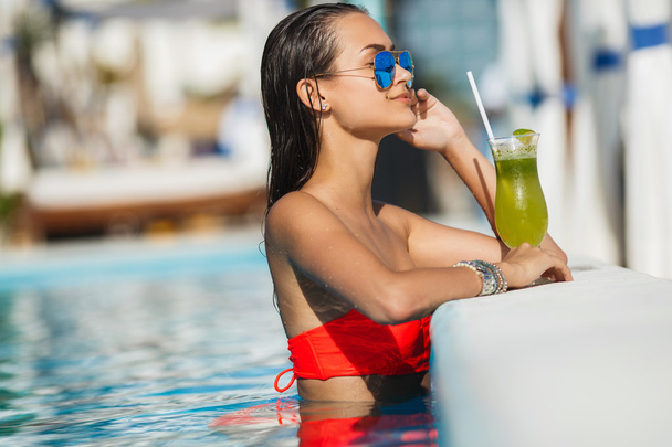 Elegant young woman in the pool with a cocktail. - Foto, Bild