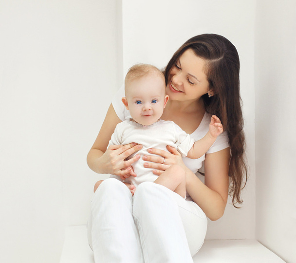 Onnellinen nuori äiti vauvan kanssa kotona valkoisessa huoneessa
  - Valokuva, kuva