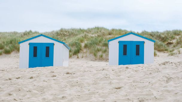 Two colorful beach huts with bright blue doors stand out against the sandy shore, creating a picturesque scene on the coast of Texel, Netherlands. - Photo, Image