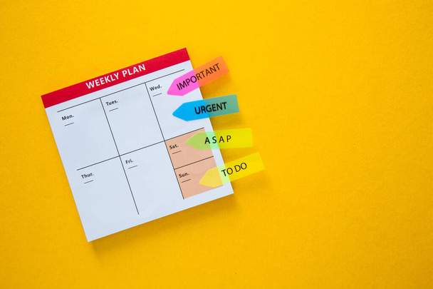 Plan semanal blanco sobre un fondo amarillo con notas adhesivas de colores brillantes para la organización - Foto, Imagen