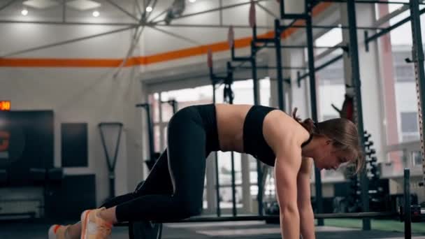 Na siłowni trener dziewczyna rzuca się na podłogę po pracy ze sztangą skacząc leżąc - Materiał filmowy, wideo