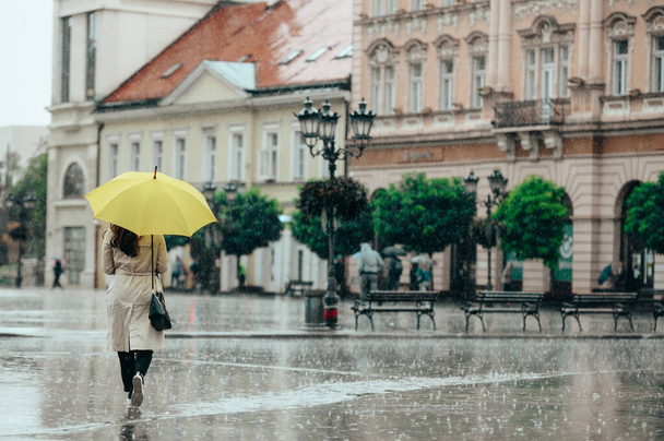 Frau mit gelbem Regenschirm bei starkem Regen in der Stadt von hinten erschossen - Foto, Bild