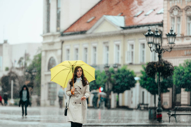 Schöne Frau trägt einen gelben Regenschirm und geht bei starkem Regen durch die Stadt - Foto, Bild