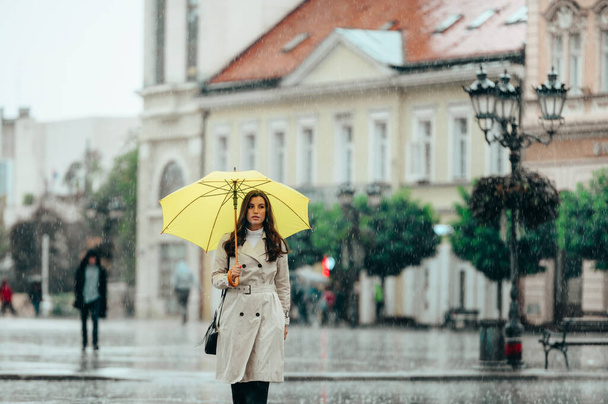 Schöne junge Frau mit einem gelben Regenschirm bei starkem Regen in der Stadt - Foto, Bild