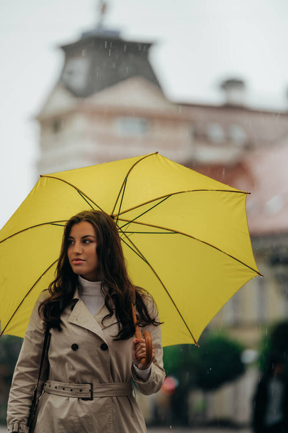 Schöne junge Frau mit einem gelben Regenschirm bei starkem Regen in der Stadt - Foto, Bild