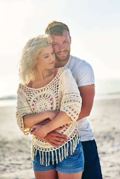 Portrait, couple and hug on beach with love for seaside romance, serene seascape and ocean with affection. Man, woman and relax for bonding by coast on weekend date, embrace and vacation with care. - Foto, Imagem