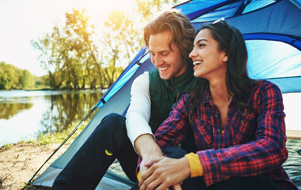Camping, holiday and couple in tent with love and happiness together on adventure in woods at lake. People, embrace or relax outdoor in nature with funny chat on vacation or travel to river in forest. - Photo, Image