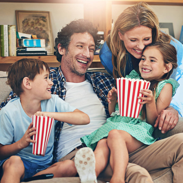 Boldog család, pihenés és nevetés popcorn kanapén vicces film, hétvége vagy nyaralás a nappaliban otthon. Anya, apa és gyerekek mosollyal a komédia, sorozat vagy streaming szolgáltatás a házban. - Fotó, kép