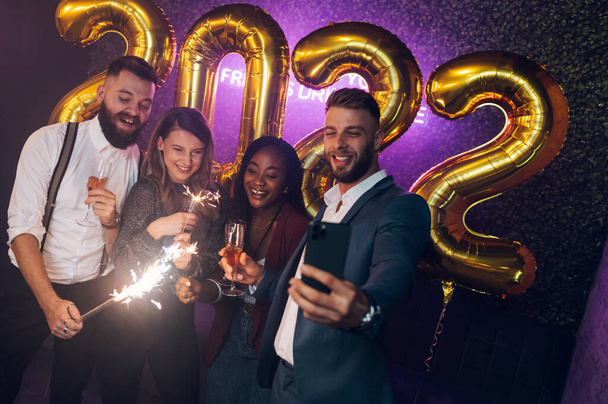 Buon gruppo di amici festeggia il Capodanno bevendo champagne in una festa in un club e scattando selfie con uno smartphone - Foto, immagini
