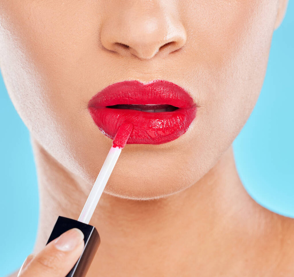 Vrouw, mond en rode lippenstift in studio, applicatie en cosmetica make-up op blauwe achtergrond. Vrouwelijke persoon, schoonheid en zelfverzekerde lippen voor glanzende verzorging, huidverzorging en make-over transformatie. - Foto, afbeelding