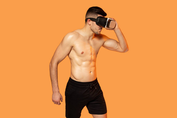 Чоловік без сорочки одягнений у гарнітуру віртуальної реальності, повністю занурений у цифровий світ. Він зосереджений на досвіді VR, без сорочки. - Фото, зображення
