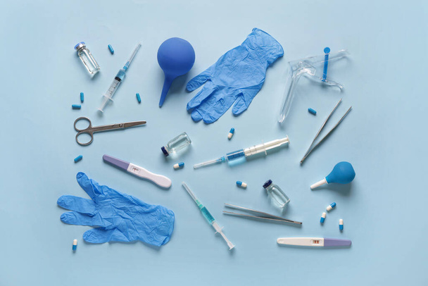 Gynekologické spekulum s těhotenskými testy, lékařské rukavice a pilulky na modrém pozadí - Fotografie, Obrázek
