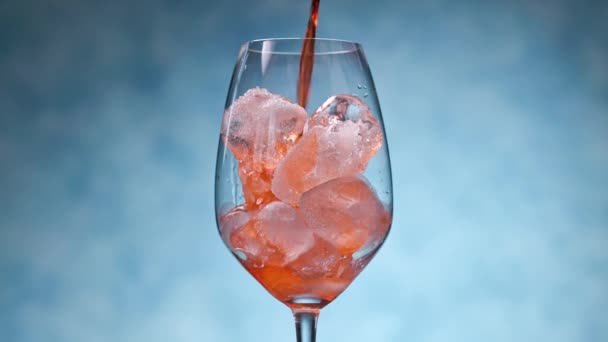 Aperol pouring on ice in wineglass on blue background. Closeup of summer drink making - Footage, Video