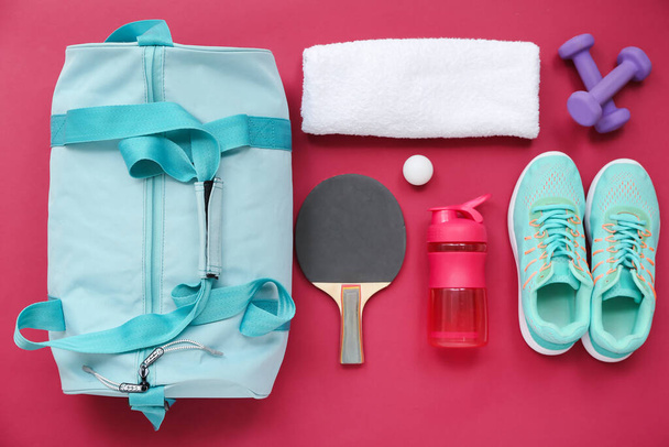Bolsa deportiva con ropa deportiva, agua y equipo de ping pong sobre fondo rojo - Foto, Imagen