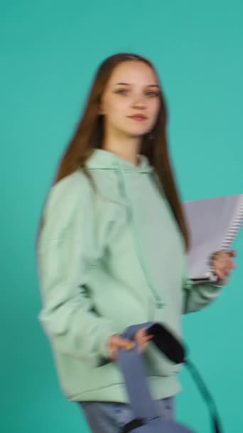 Vídeo vertical Retrato de mujer sonriente con mochila sosteniendo cuaderno de la escuela y notas, aislado sobre fondo del estudio. Chica alegre con útiles escolares en armas, preparándose para ir a la universidad - Imágenes, Vídeo