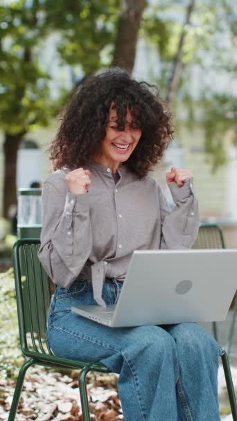 Happy Caucasian młoda kobieta pracująca na laptopie krzyczy w triumfie wygrać świętując dobrą wiadomość wiadomość sukces gry kasyno loterii pieniądze jackpot zwycięstwo odkryty. Dziewczyna z miejskiej ulicy. Pionowe - Materiał filmowy, wideo
