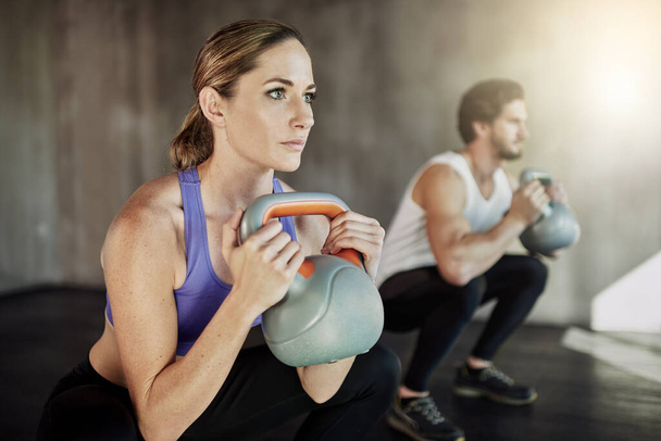 Power, squat and couple in gym with kettlebell, fitness training and workout challenge together at sports club. Man, woman or personal trainer with muscle development, healthy body and exercise - Foto, imagen