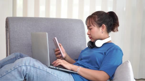 Krásná šťastná usměvavá asijská žena sedí relaxující na pohodlné pohovce v obývacím pokoji pomocí notebooku. Nakupovat online, číst zprávy, pracovat pohodlně z domova. - Záběry, video
