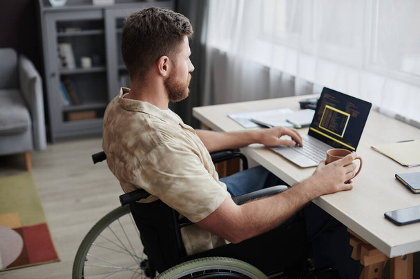 Side view portrait of bearded man with disability using computer while working from home in IT career - Photo, Image