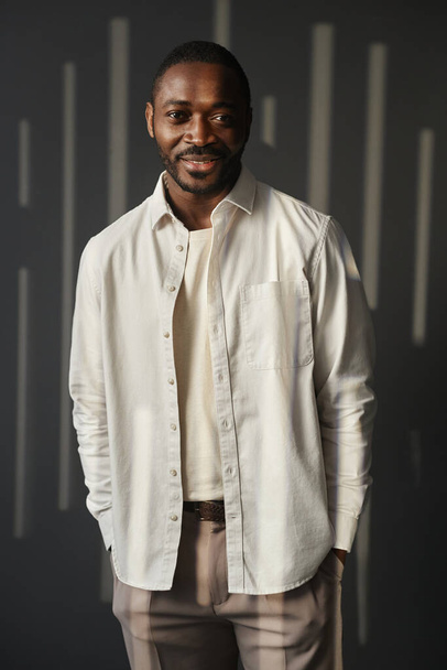 Vertical portrait of charismatic Black man smiling at camera standing against light and shadow background - Photo, Image