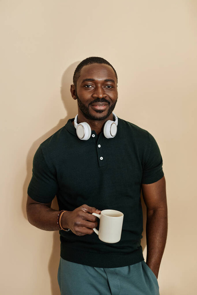 Vertikales Porträt eines gut aussehenden erwachsenen afroamerikanischen Mannes, der vor neutralem Hintergrund mit einer Tasse Kaffee steht - Foto, Bild