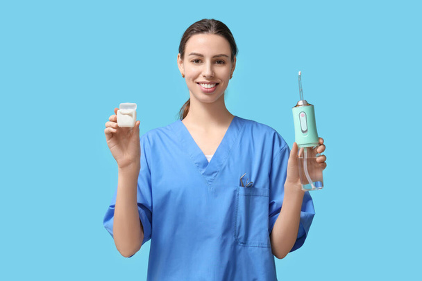 Naispuolinen hammaslääkäri suukastelulaitteella ja hammaslangalla sinisellä pohjalla - Valokuva, kuva