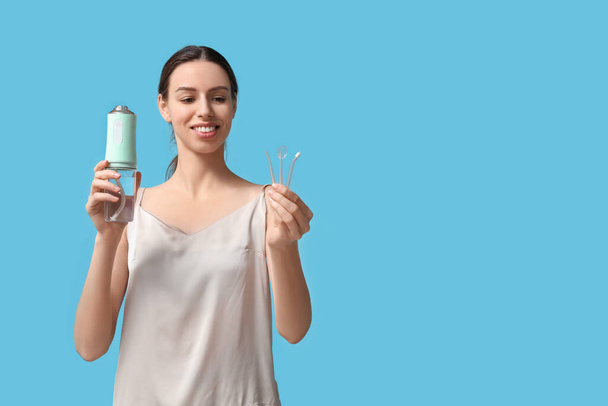 Beautiful young woman with oral irrigator on blue background - Photo, Image