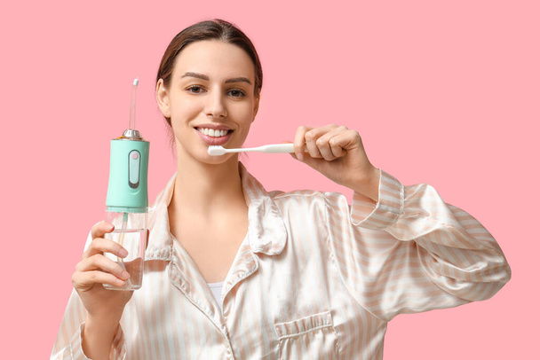 Beautiful young woman with oral irrigator and toothbrush on pink background - Photo, Image