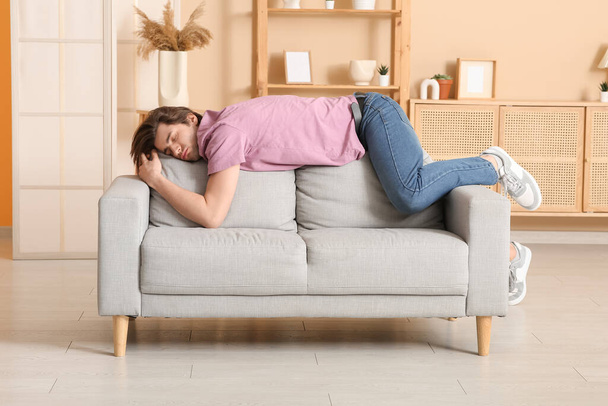 Уставший молодой человек спит дома на диване - Фото, изображение