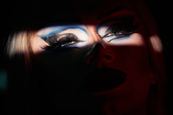Spotlight detail shot van drag queen performer op het podium met focus op ogen met extravagante make-up, kopieer ruimte - Foto, afbeelding