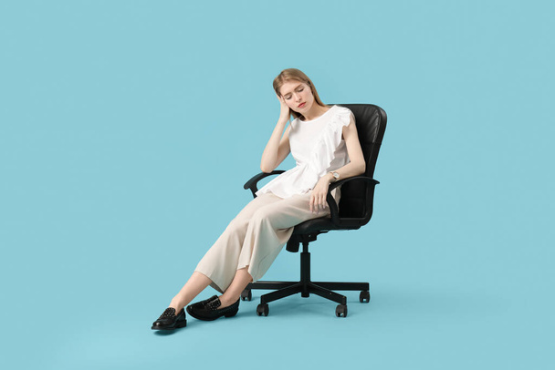 Moe jonge vrouw zitten op kantoor stoel tegen blauwe achtergrond - Foto, afbeelding